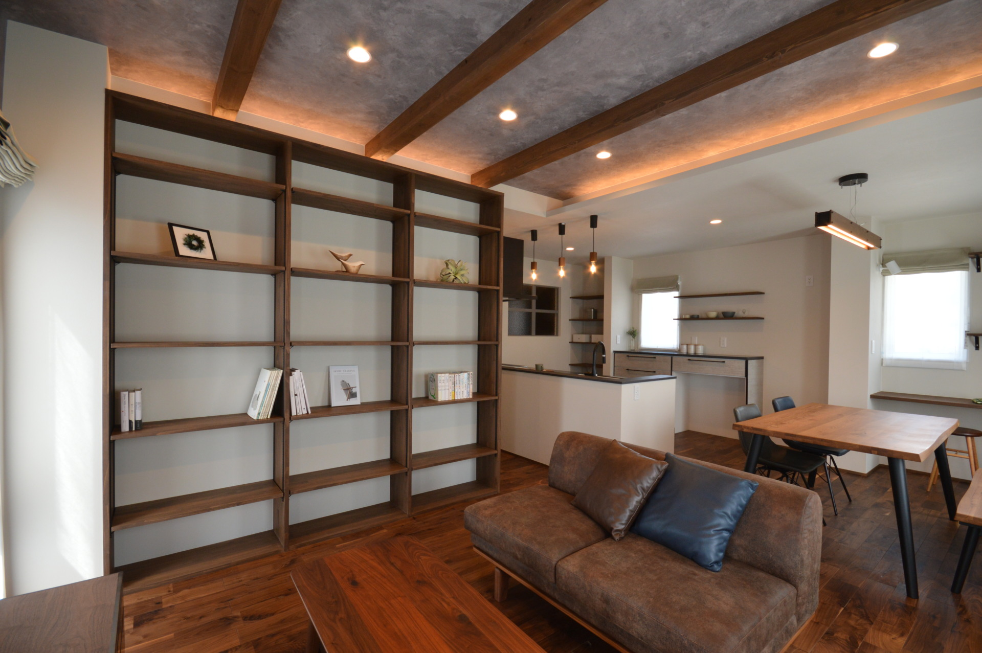 造作大型本棚のあるリビングの間接照明｜天井梁とモルタル調壁のある注文住宅